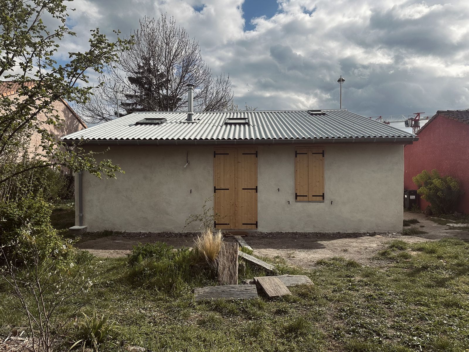 Façade entièrement enduite à la chaux, volets bois et toiture en bac acier