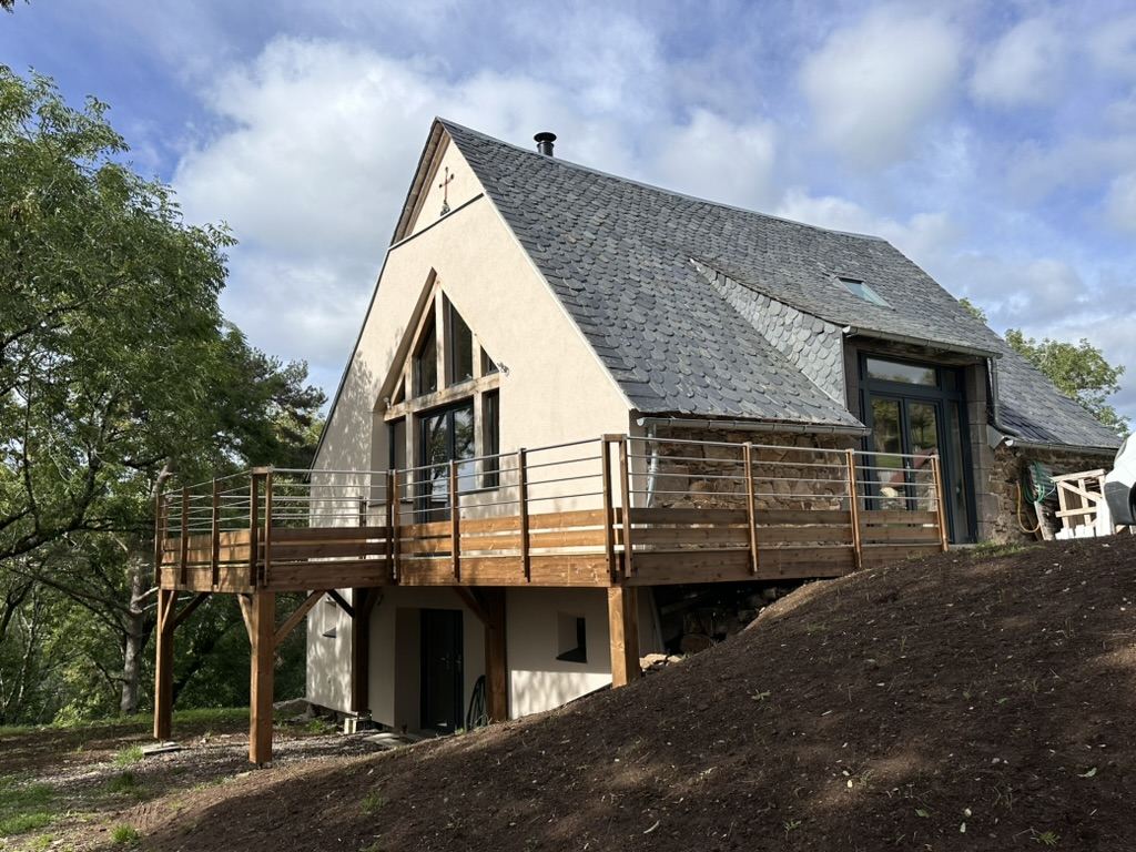 Façade de la grange rénovée avec sa terrasse en bois, toiture en ardoise écaille
