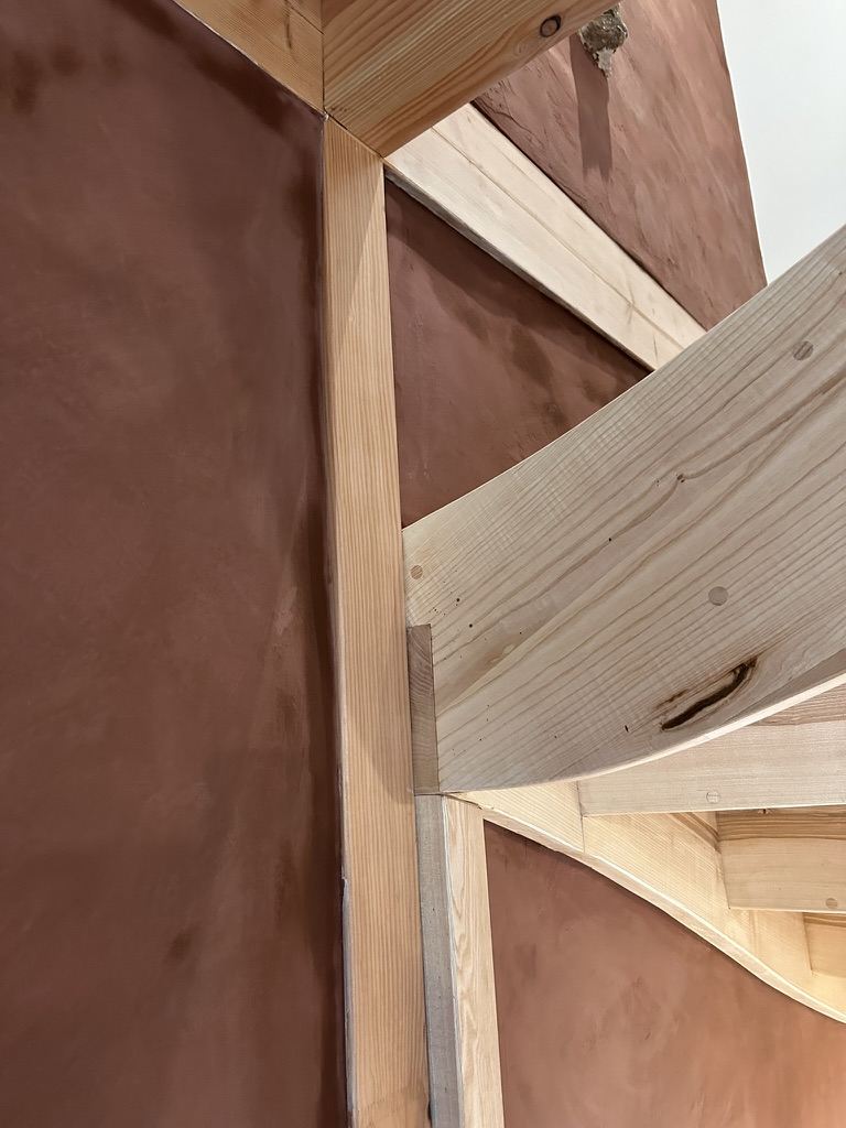 Détail d'angle : mur patiné terracotta et charpente bois neuve